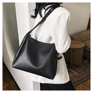 Side view of black large leather tote bag worn by a model in a minimalist room