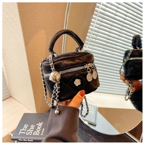 Détail du mini sac seau en cuir noir matelassé avec breloque camélia et chaîne argentée
