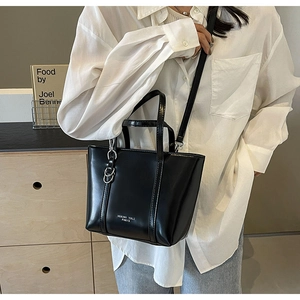 Detail of black tote bag featuring silver D-ring hardware and brand text on shoulder