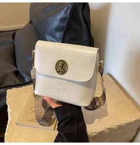 Détail du sac en cuir PU blanc crème avec emblème d'ours doré et large bandoulière