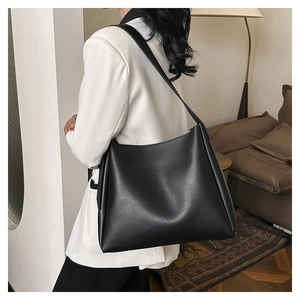 Minimalist black matte leather bucket bag with wide strap on a female model in a home setting