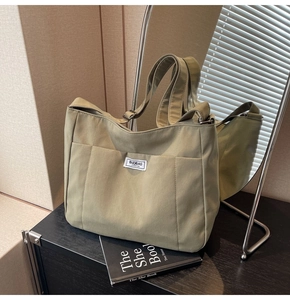 Detail view of sage green canvas tote bag showing the stylish logo patch and wide strap