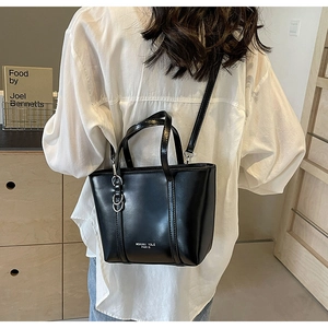 Detail shot of a black leather tote bag featuring adjustable strap and white brand lettering