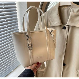 Detail of a minimalist cream tote bag showing the logo and polished synthetic leather texture