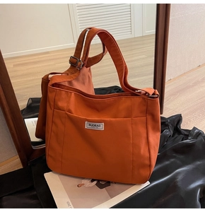Detail of orange canvas tote bag showing the fashion label and spacious front pocket