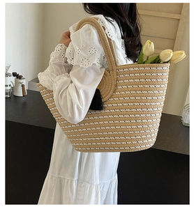 Close-up of woven straw tote bag with black tassel detail and striped knit texture
