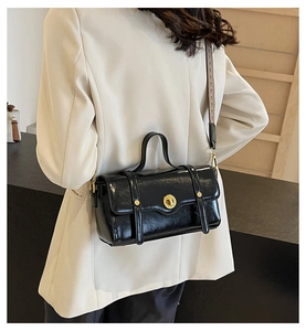 Close-up of a glossy black crossbody bag featuring a golden twist lock and woven strap