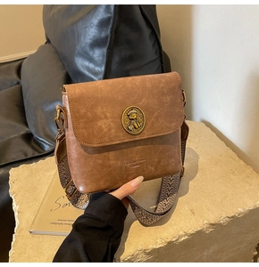 Détail d'un sac bandoulière marron avec boucle ours dorée et bandoulière tissée large