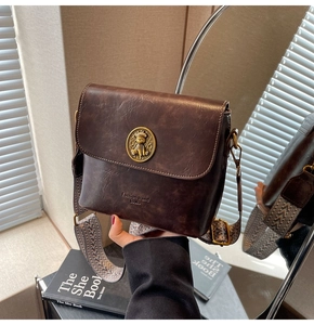 Détail du sac seau en cuir marron foncé avec emblème d'ours doré et bandoulière tissée