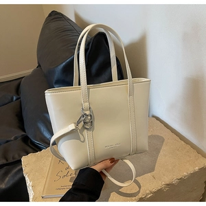 Detail of off-white PU leather tote with silver Logo and adjustable strap on stone surface