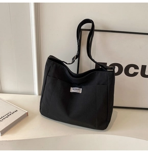 Detail of black canvas tote bag showing the fashion label and adjustable shoulder strap