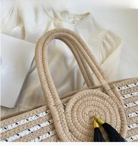 Close-up of woven straw tote bag handle with stylish black tassel and metallic accents