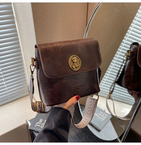 Détail d'un sac seau vintage en cuir marron avec emblème d'ours et large bandoulière