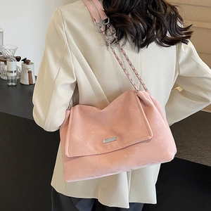 Pink suede tote bag with chain strap shown on model in a modern cafe setting
