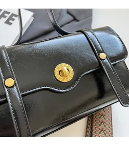 Detail of black leather crossbody bag with golden Roman numeral lock and woven strap