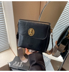 Détail du sac seau noir avec emblème d'ours doré et large bandoulière jacquard