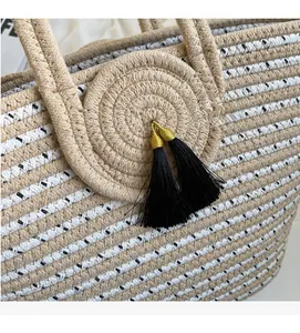 Detail of woven straw tote bag featuring contrast patterns and black tassel with gold thread