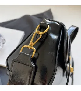 Close-up of premium gold metal hook on black glossy leather crossbody bag surface