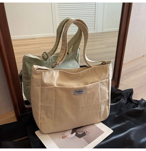 Detail view of canvas tote bags in beige and green with adjustable straps and logo patch