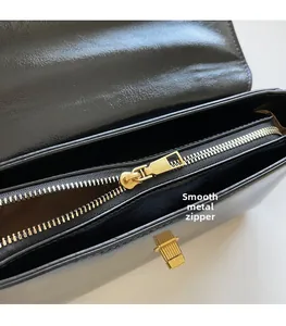 Close-up of smooth gold metal zipper and internal compartment on black leather bag