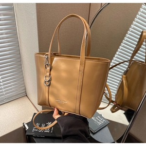 Detail of brown leather tote bag featuring dual handles and silver chain ornament