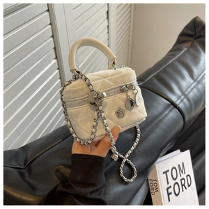 Détail d'un mini sac seau blanc matelassé avec bandoulière chaîne et breloque camélia
