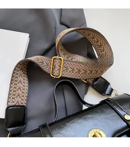 Detail of adjustable woven shoulder strap on a glossy black crossbody bag with gold buckle