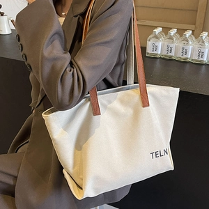 Minimalist off-white canvas tote bag with brown leather straps worn by a model