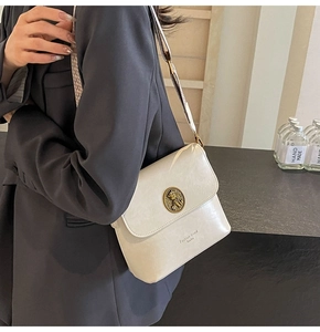 Détail d'un sac seau en cuir crème avec boucle chat vintage dorée et bandoulière large