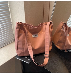 Close-up of coral pink nylon tote bag showing texture, logo patch and adjustable strap
