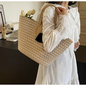 Detail of a large woven straw tote with striped pattern and a decorative black tassel