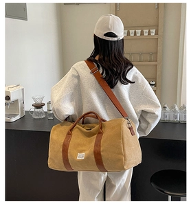 Back view of model wearing a large khaki canvas travel bag with brown leather straps