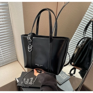 Detailed shot of black tote bag with silver chain accessory and branded logo on the side