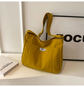 Detail of a bright yellow canvas tote bag featuring a side pocket and stitched label