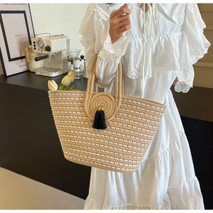 Detail of woven straw tote bag with black tassel charm in a cozy lifestyle setting
