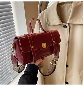 Detail of burgundy leather crossbody bag with wide geometric patterned strap and gold hardware