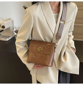 Détail du sac seau en cuir marron avec emblème lion doré et bandoulière tissée large