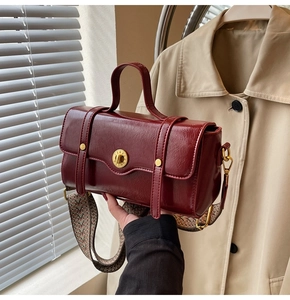 Detail of vintage burgundy crossbody bag with ornate gold buckle and patterned wide strap