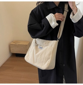 Close-up of minimalist cream canvas crossbody tote with adjustable strap and front pocket