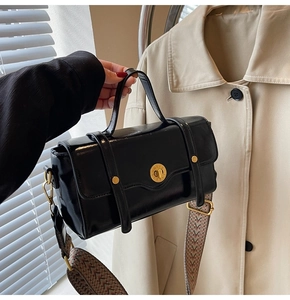 Close-up of black glossy leather bag featuring retro gold hardware and woven wide strap