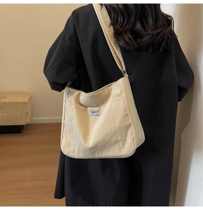 Detail of off-white canvas tote bag with side pocket and small fabric label on black coat