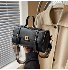 Detail of black faux leather handbag with golden round lock and ethnic woven strap