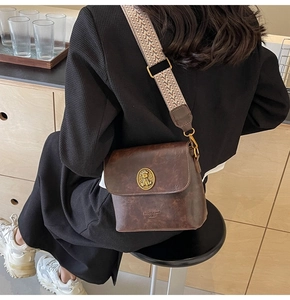 Détail du sac seau vintage marron avec bandoulière tissée et emblème doré