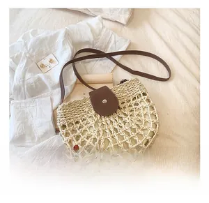 Detail of the woven straw texture and brown leather flap with metal buckle on the crossbody bag