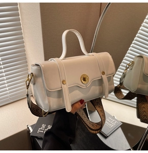 Close-up of white crossbody bag with golden roman lock and woven shoulder strap