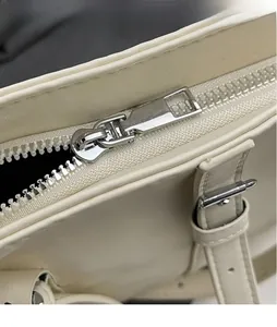 Détail de la fermeture éclair en métal argenté sur un sac en similicuir blanc crème