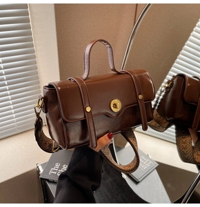 Detail of vintage brown leather handbag with gold metal lock and patterned wide strap
