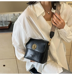 Détail du sac seau en cuir noir avec large bandoulière géométrique et boucle dorée