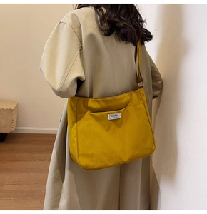 Close-up of yellow canvas tote bag with front pocket and logo label on beige coat