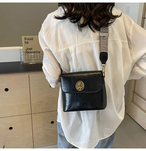 Détail du sac seau noir avec emblème doré et large bandoulière à motifs variés